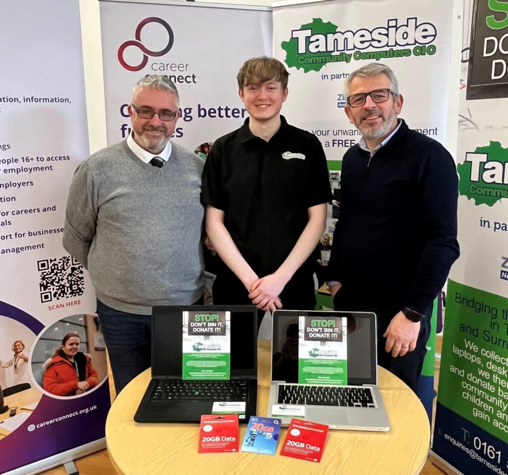 Two Career Connect employees and one Tameside Community Computers employee stood smiling in front of two pull up banners from each company