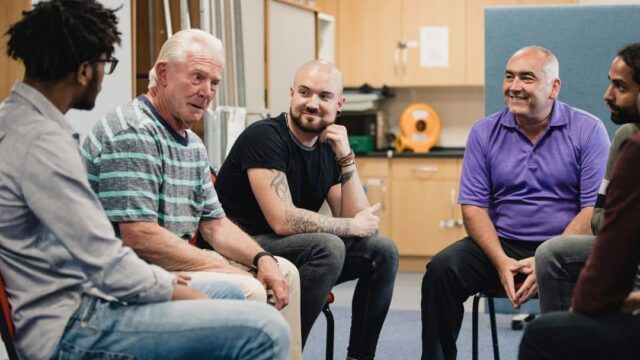 A group of men sitting in a discussion group, providing support to one another.