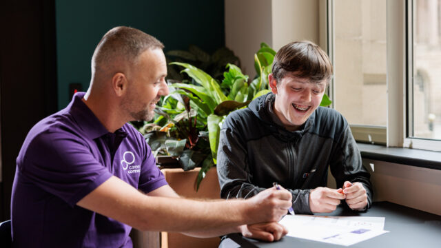 A teenage boy is sat next to his male careers adviser, who is helping him to fill in an action plan.