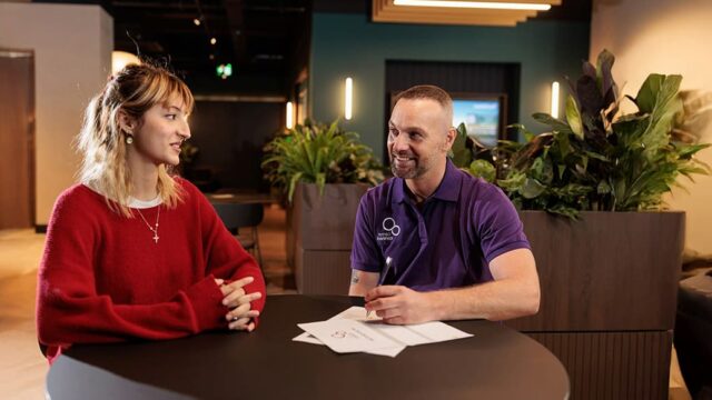 Careers adviser Paul sat smiling at a desk with a young woman he is supporting