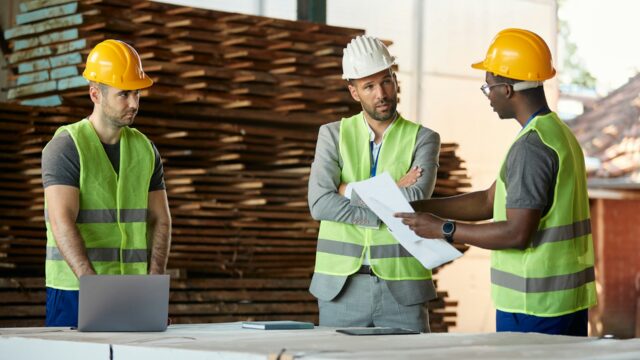 3 men wearing Hi-Vis jackets and hard hats on a construction site discussing plans