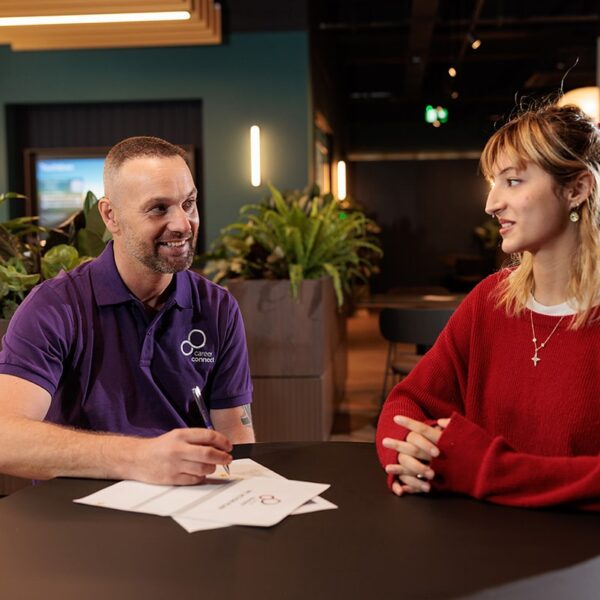 Careers adviser Paul sat smiling at a desk with a young woman he is supporting