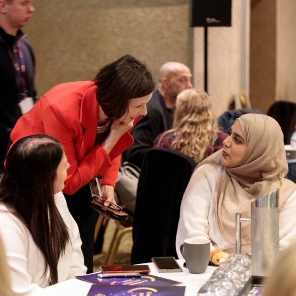 A woman standing talking to two women sat down at an event