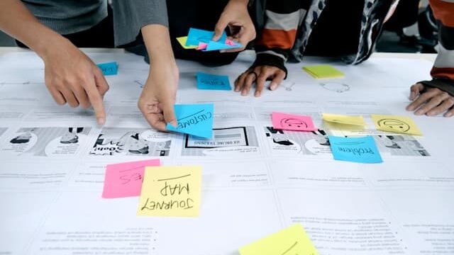 A group of three people leaning over some work placing different colour sticky notes on the work.