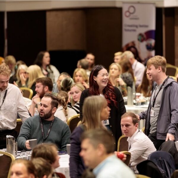 A group of people in discussion and smiling in a room full of people at an event