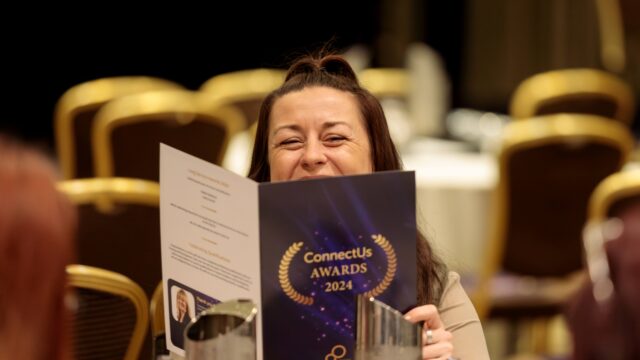 A woman sat at a table holding a programme for the ConnectUs awards 2024