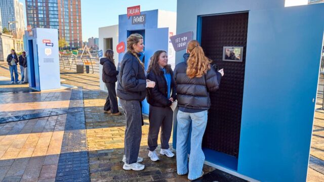 Three young women in Manchester outside a blue booth where they can call a careers adviser