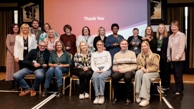 A group photo of our staff award winners. Some are sat down and some stood up, and many of them are holding their trophies.