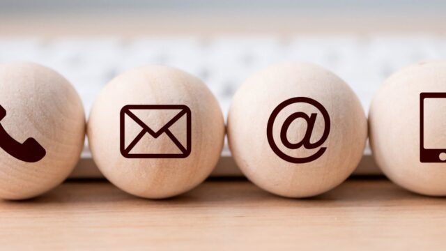 4 light coloured wooden balls each with a different icon on it. From left to right there is a phone icon, envelope icon, @ sign, mobile icon.