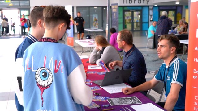 A career connect adviser sat at a stall in a local community venue, answering questions from two young people.