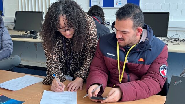 A female Career Connect adviser is helping a young man fill in a form.