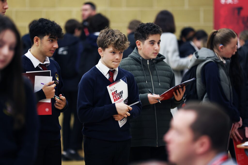 three male students holding booklets that say "get future ready" whilst at a careers fair
