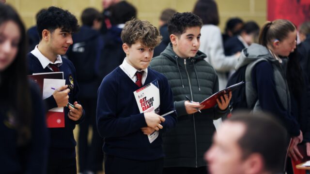 three male students holding booklets that say "get future ready" whilst at a careers fair