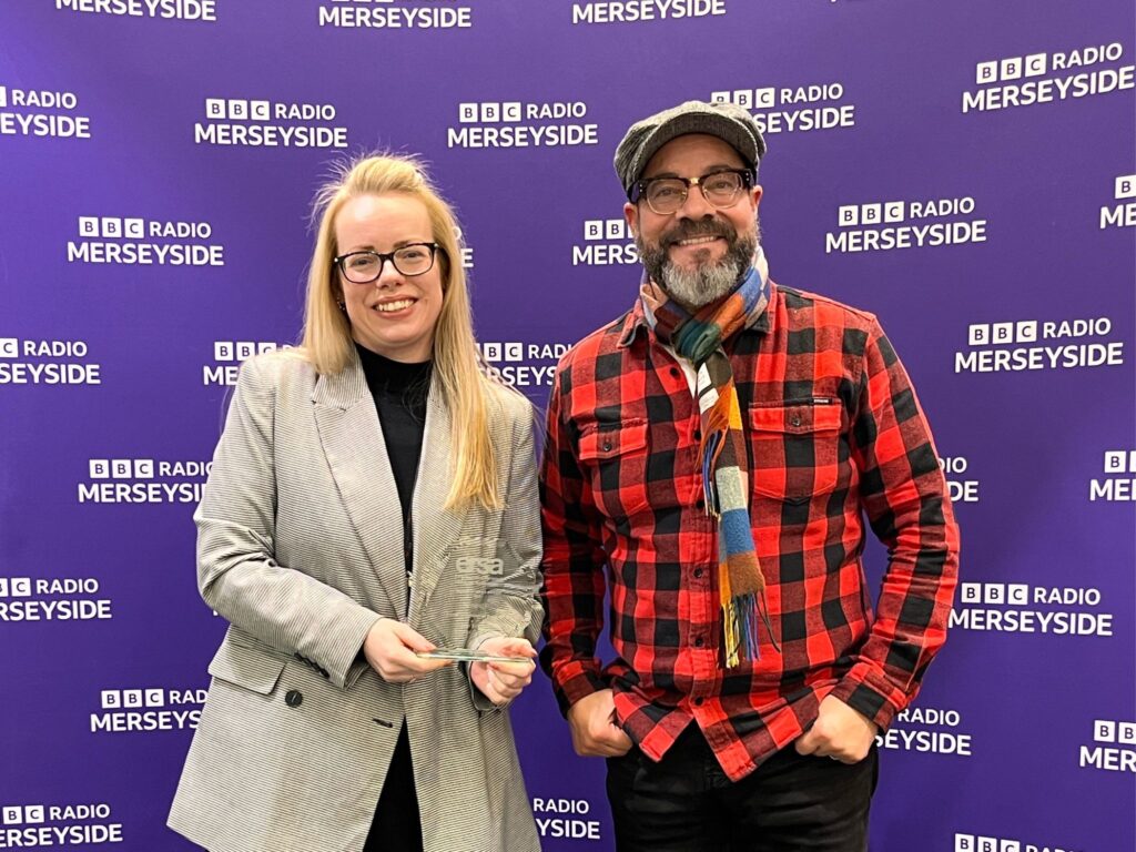 Katie Enstone with her ERSA award next to BBC Radio Merseyside presenter in front of a banner with the BBC Radio Merseyside logo on
