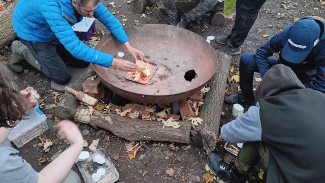 A team instructors showing young people how to safely light a fire in a special metal brazier.