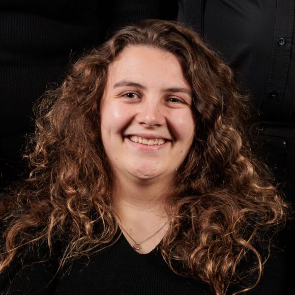 Head and shoulders shot of Rachel. She has curly brown hair and a black top. She is smiling.