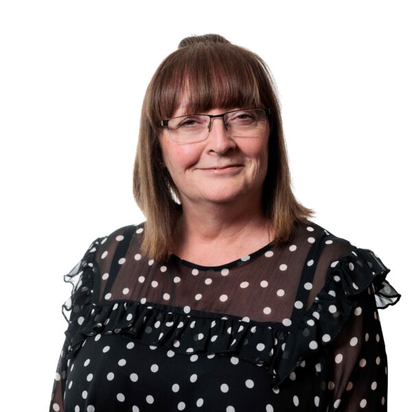 head and shoulders shot of Sue Dickinson. She is wearing a black top with white spots and glasses. She has shoulder length brown hair and is smiling at the camera.