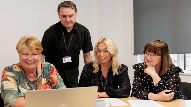 Members of Career Connect's training team delivering a course. Three women are at a desk, with a laptop in front of them. They are explaining course content to a male colleague who is standing up.