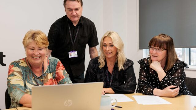Members of Career Connect's training team delivering a course. Three women are at a desk, with a laptop in front of them. They are explaining course content to a male colleague who is standing up.