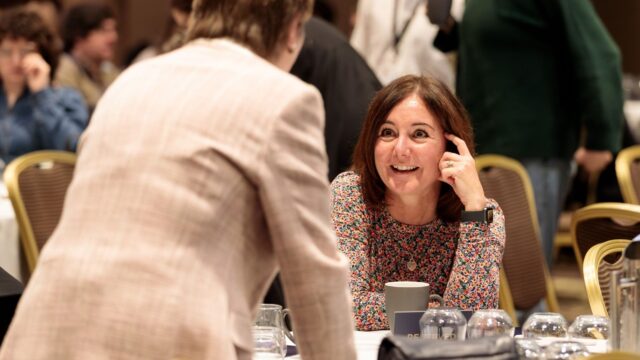 Two Career Connect trustees having a conversation at a table at the ConnectUs event. One trustee is stood up and one is sat down.