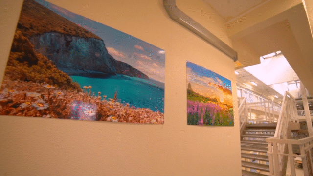 Inside a prison wing. There are stairs to the next level, and pictures of landscapes of sea and fields on the wall.