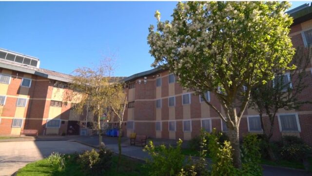 The outside of a prison on a sunny and clear day with trees in front of the building