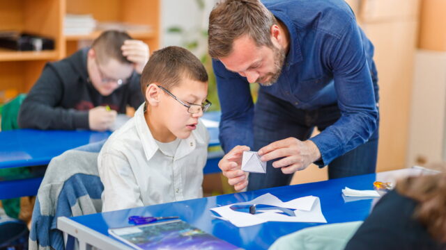Special education teacher holding a model made by intellectually challenged elementary student, looking satisfied with his accomplishment