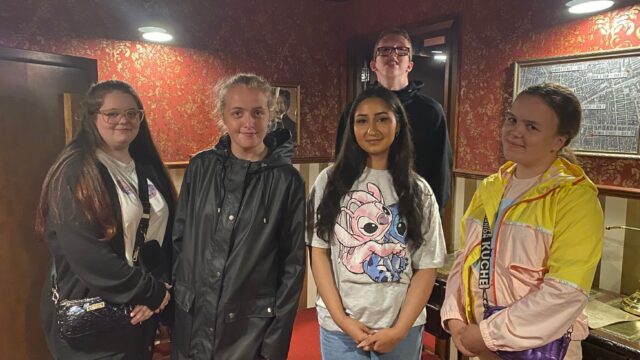 A group of five Youth Ambassadors in an escape room as part of their enrichment activities. They are all smiling at the camera.