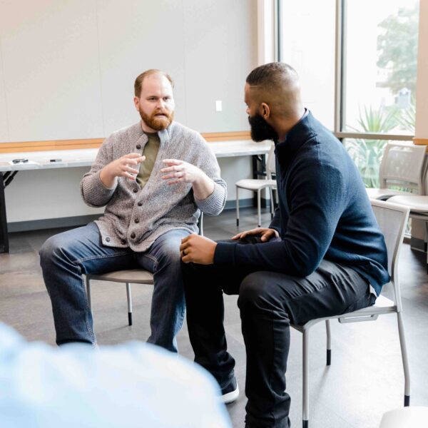 Two men, sitting and having a discussion in a large room.