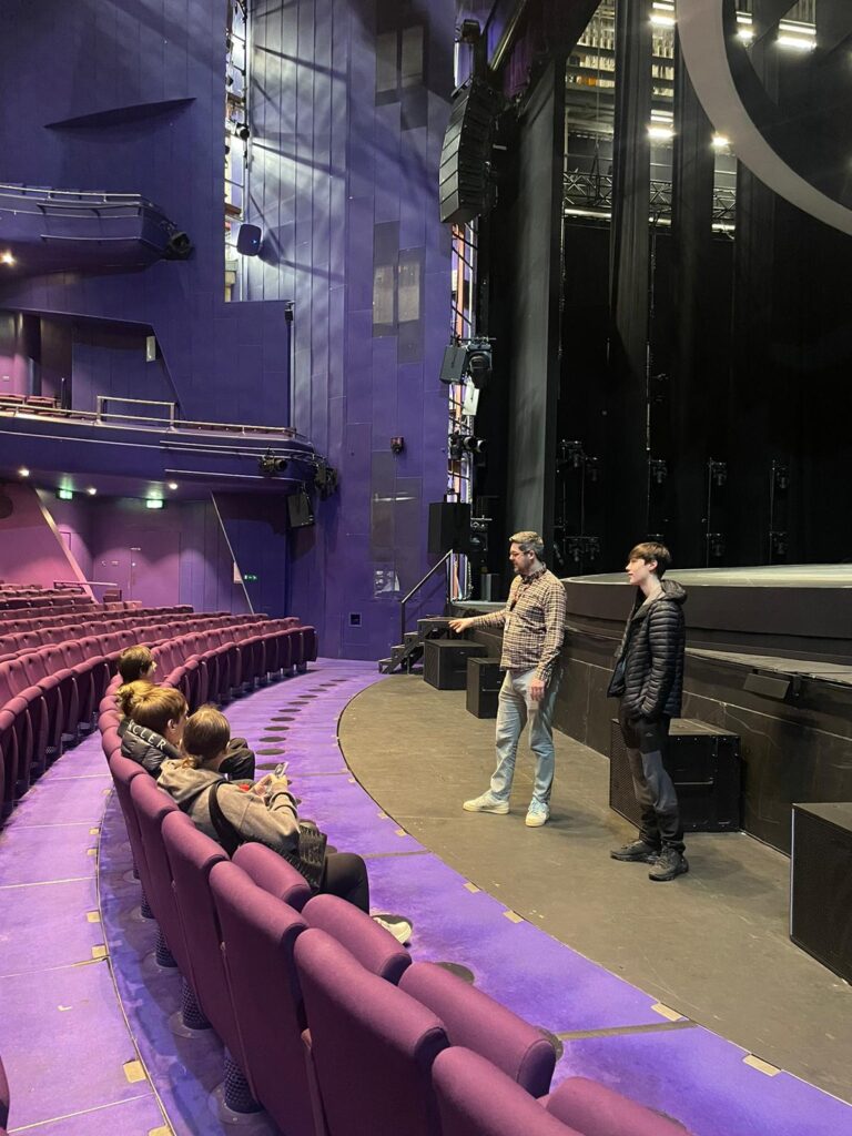 A group of young people sit in the auditorium at the Lowry as part of a tour of the venue to explain the careers available there.