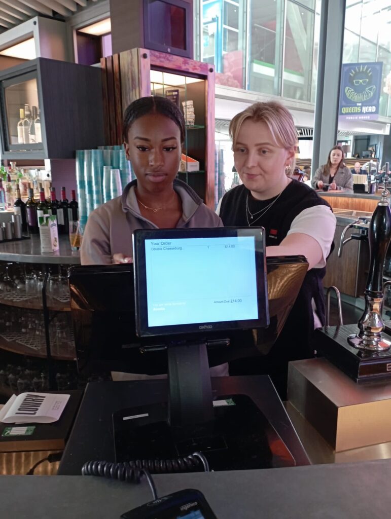 Two young women, working at till in a bar.