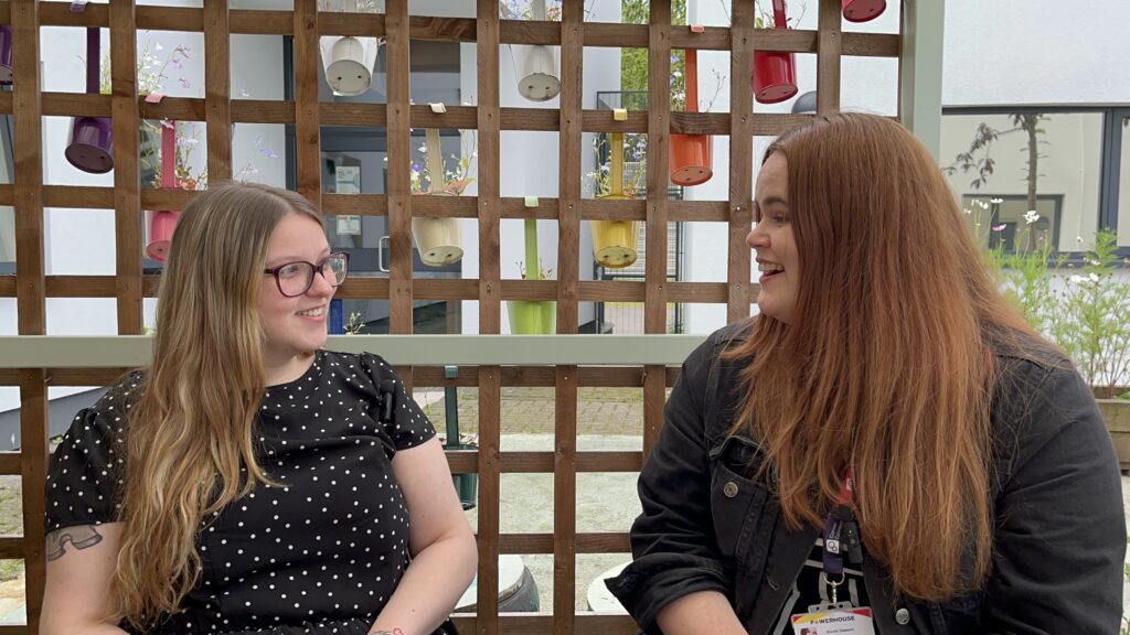 A female young person with long blond hair and glasses in conversation and laughing with their female careers adviser who has long auburn hair.