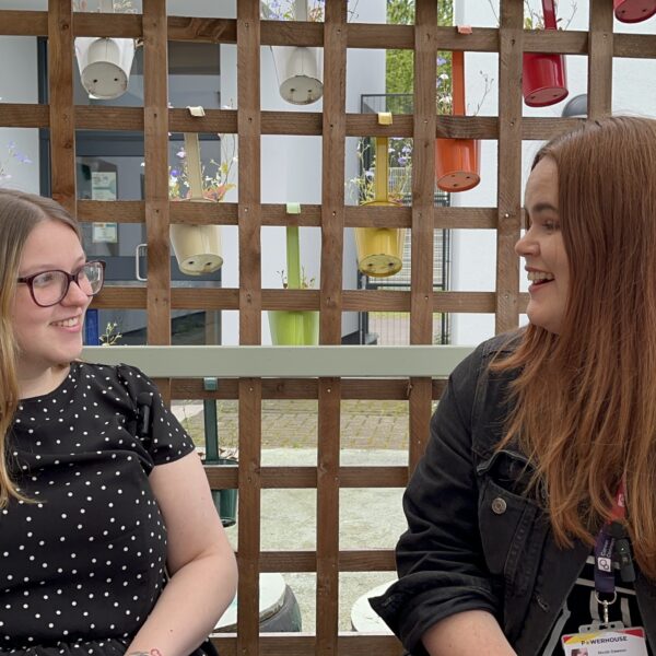 A female young person with long blond hair and glasses in conversation and laughing with their female careers adviser who has long auburn hair.