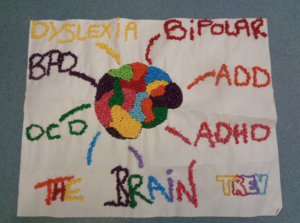 A hand-made poster using coloured pellets featuring the title "The Brain" and a drawing of the human brain with labels: dyslexia, BPD, bipolar, ADD, ADHD, and OCD. It is signed with the name "Trev".