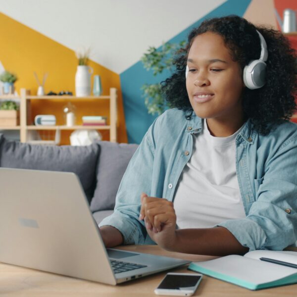 A black teenage girl at a laptop wearing headphones and on a video call. Image credit: Vitaly Gariev, unsplash