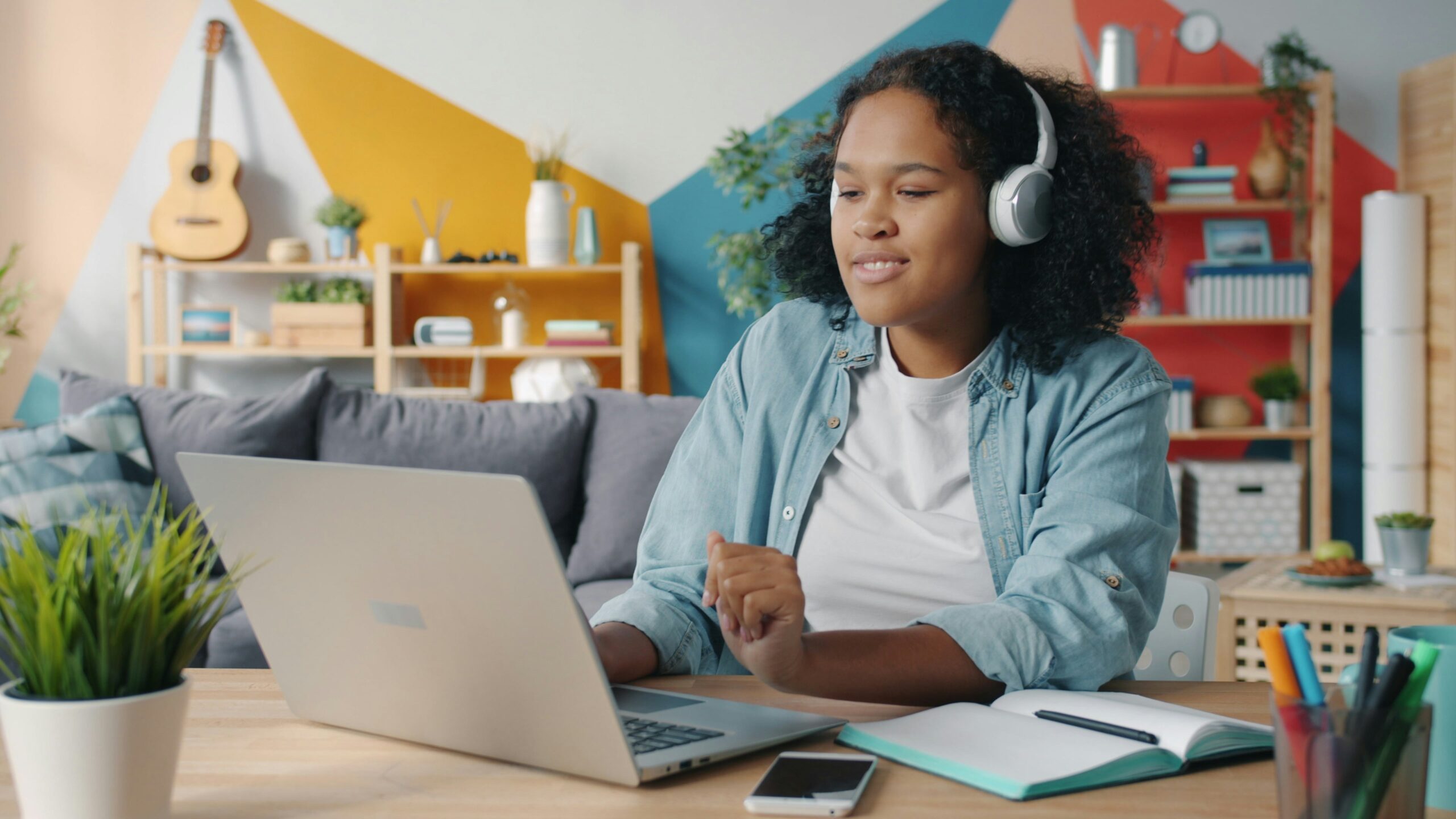 A black teenage girl at a laptop wearing headphones and on a video call. Image credit: Vitaly Gariev, unsplash