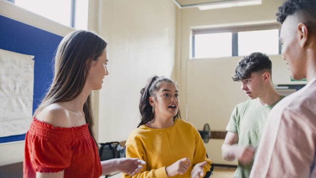 A group of young people talking together in a white room.
