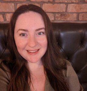 A head and shoulders photo of Megan Jezzard, careers adviser in our schools team. Megan is sitting on a couch against a brick wall. She has long dark hair and is smiling.