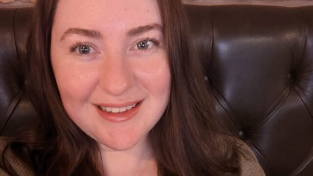 A head and shoulders photo of Megan Jezzard, careers adviser in our schools team. Megan is sitting on a couch against a brick wall. She has long dark hair and is smiling.