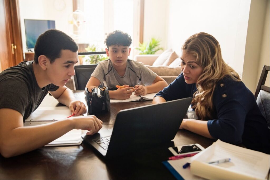 A woman teaching two young boys using a computer in a home environment.