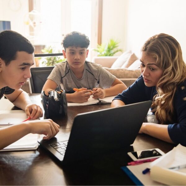 A woman teaching two young boys using a computer in a home environment.