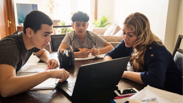 A woman teaching two young boys using a computer in a home environment.