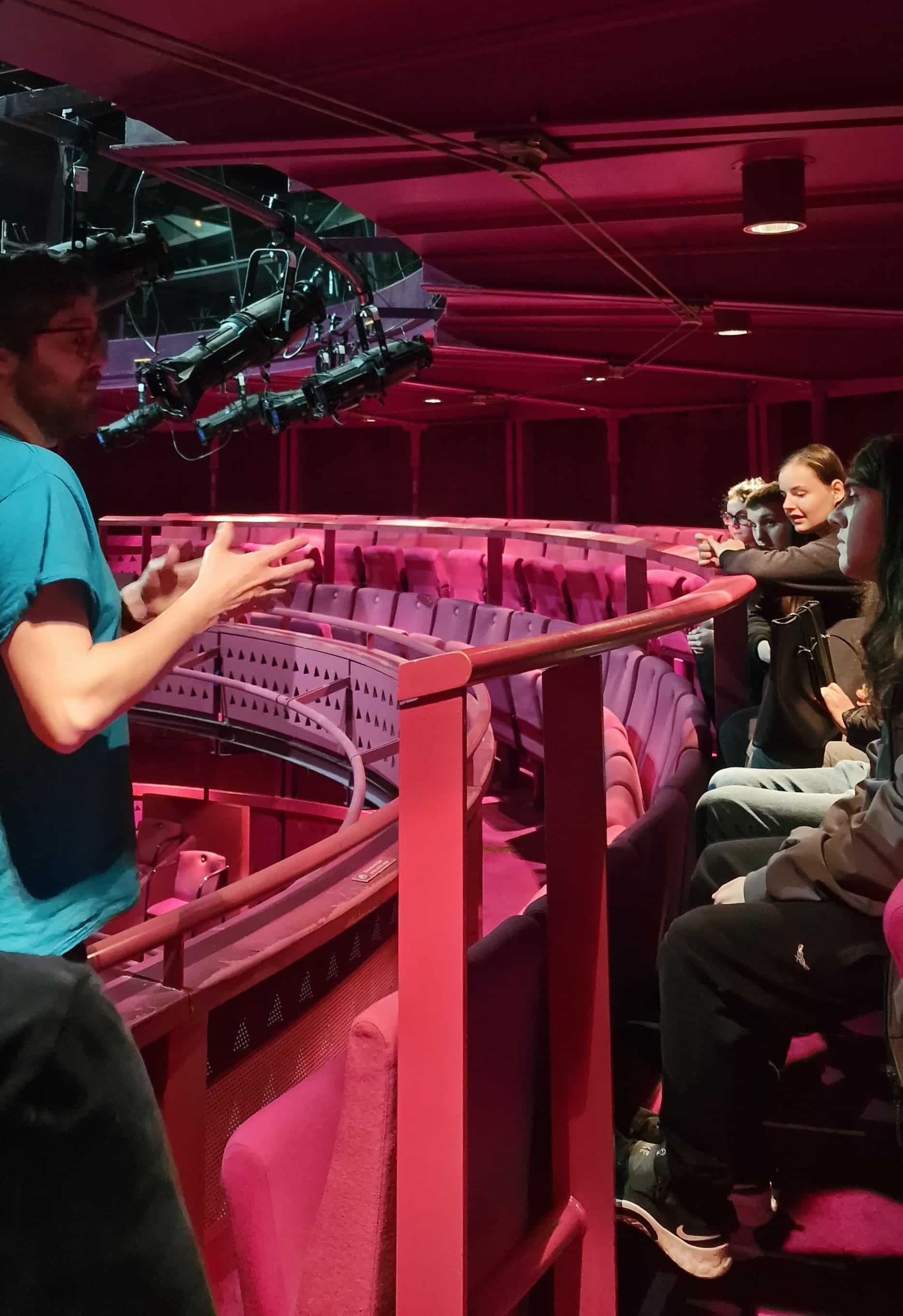 A member of staff from the Lowry is standing in the auditorium of the Lowry, talking to young people on the Discover Your Future programme. 