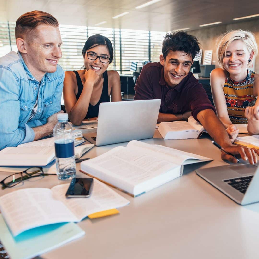 A group of students sitting around a table studying with books and a laptop.