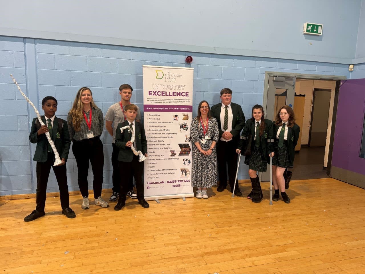 A group of school students standing in a row with a teacher and an employer. They are holding a tinfoil tower as part of a team building and enterprise event.