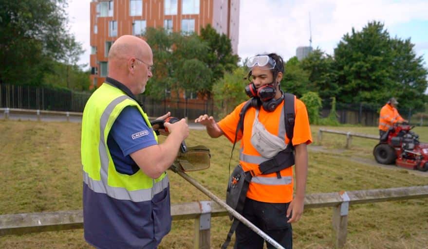 A young person is carrying out landscaping work in a neighbourhood in Manchester. He is being given some ear defenders from his supervisor. 