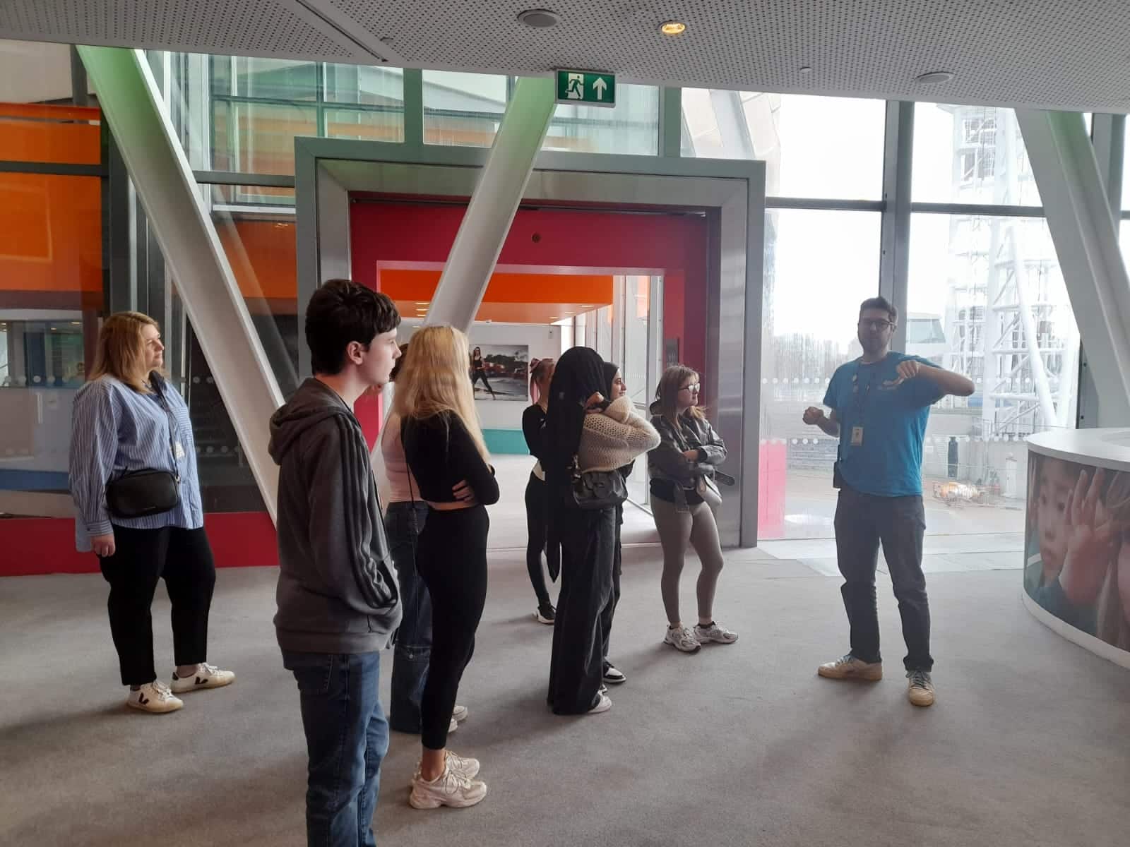 A group of young people in the foyer of the Lowry, being given a tour by a member of staff