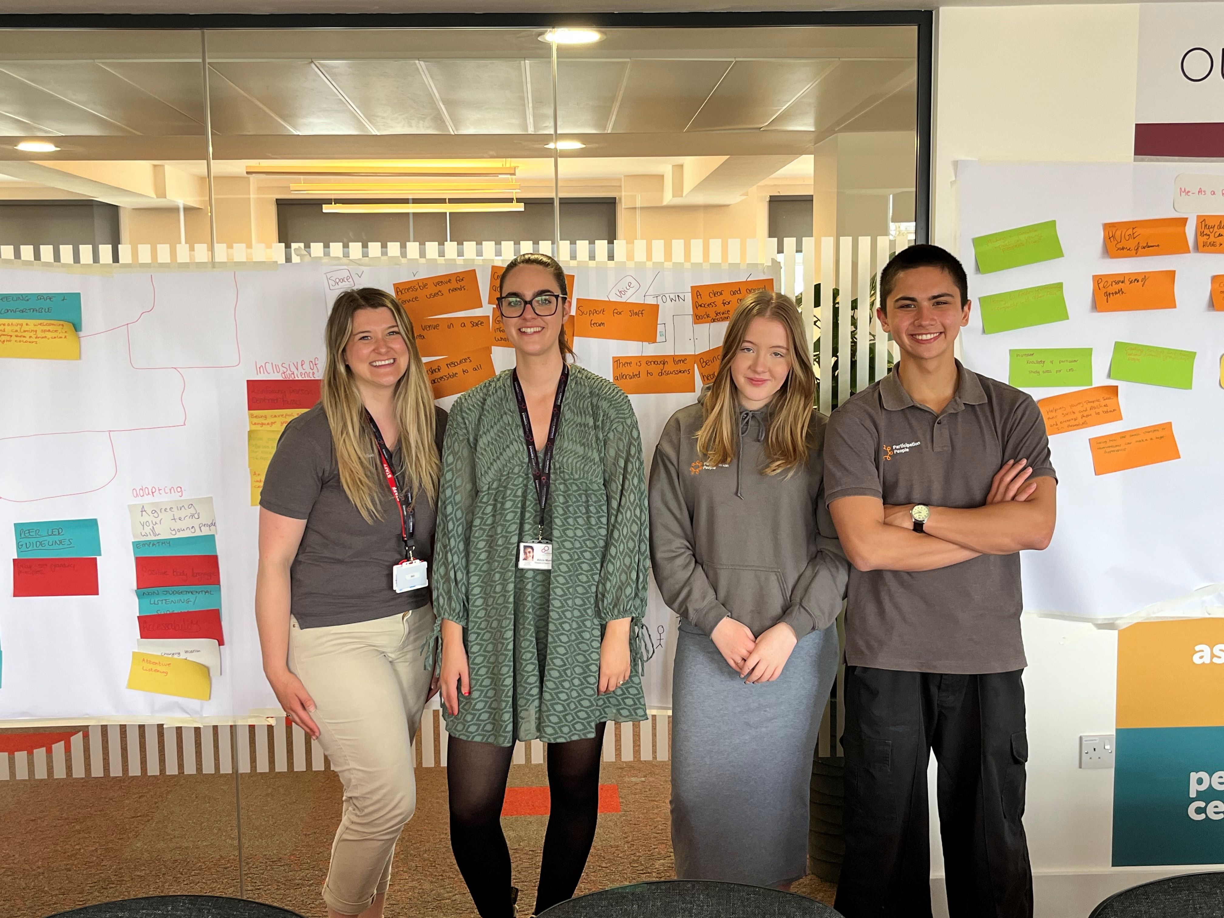 career connect and participation people staff stand against a wall smiling. behind them on the wall are multicoloured post it notes from workshop, with ideas about how best to support young people. 